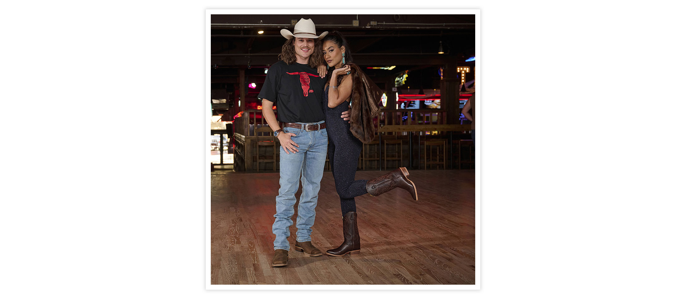 A man wearing 1879 modern slim mens jeans in blue and men’s cowboy live on Tee in black posing next to a woman holding a coat.